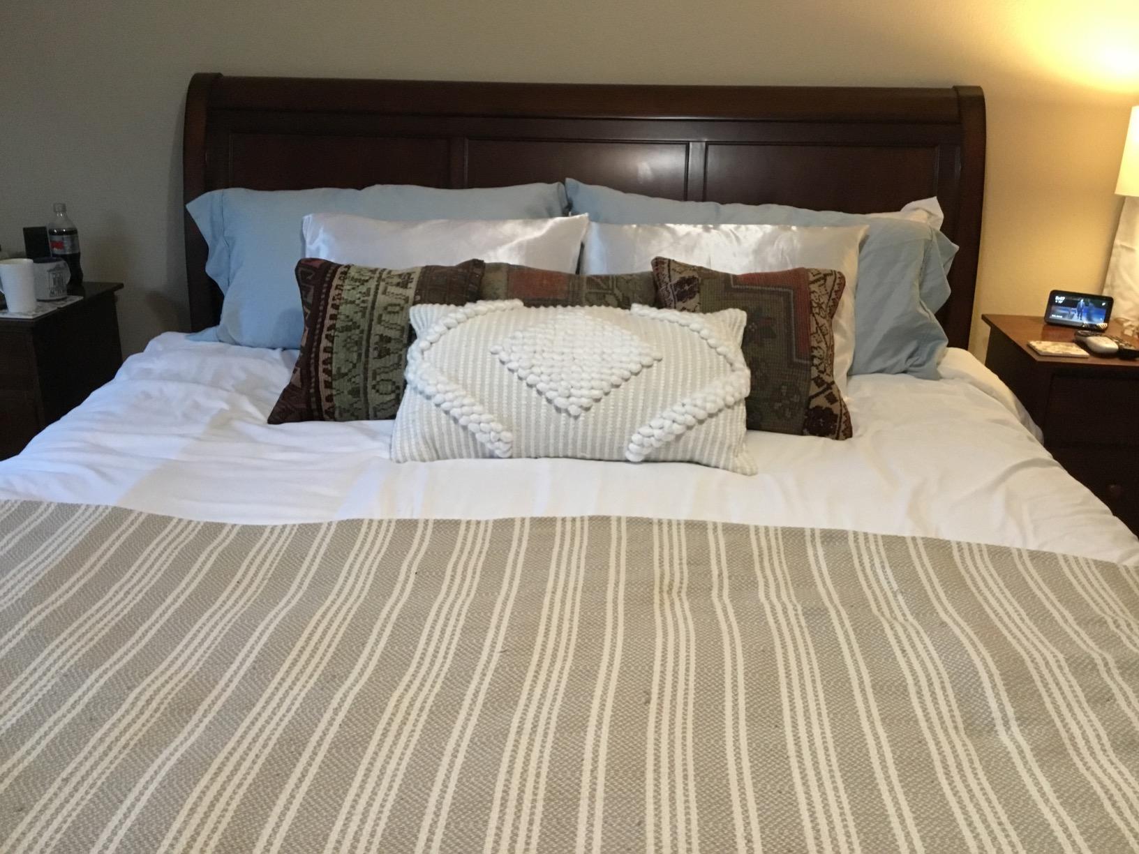 A made bed with beige and white striped decorative pillows and a knitted throw in a cozy bedroom interior.