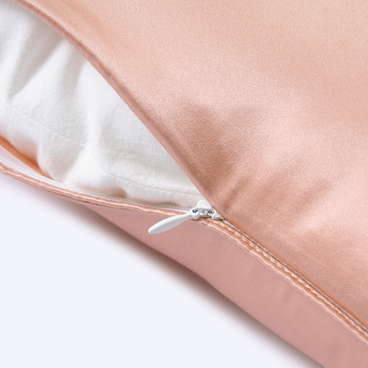 A pink mulberry silk cushion pillowcase with a zipper, partially unzipped to show the inner lining, on a plain studio backdrop.