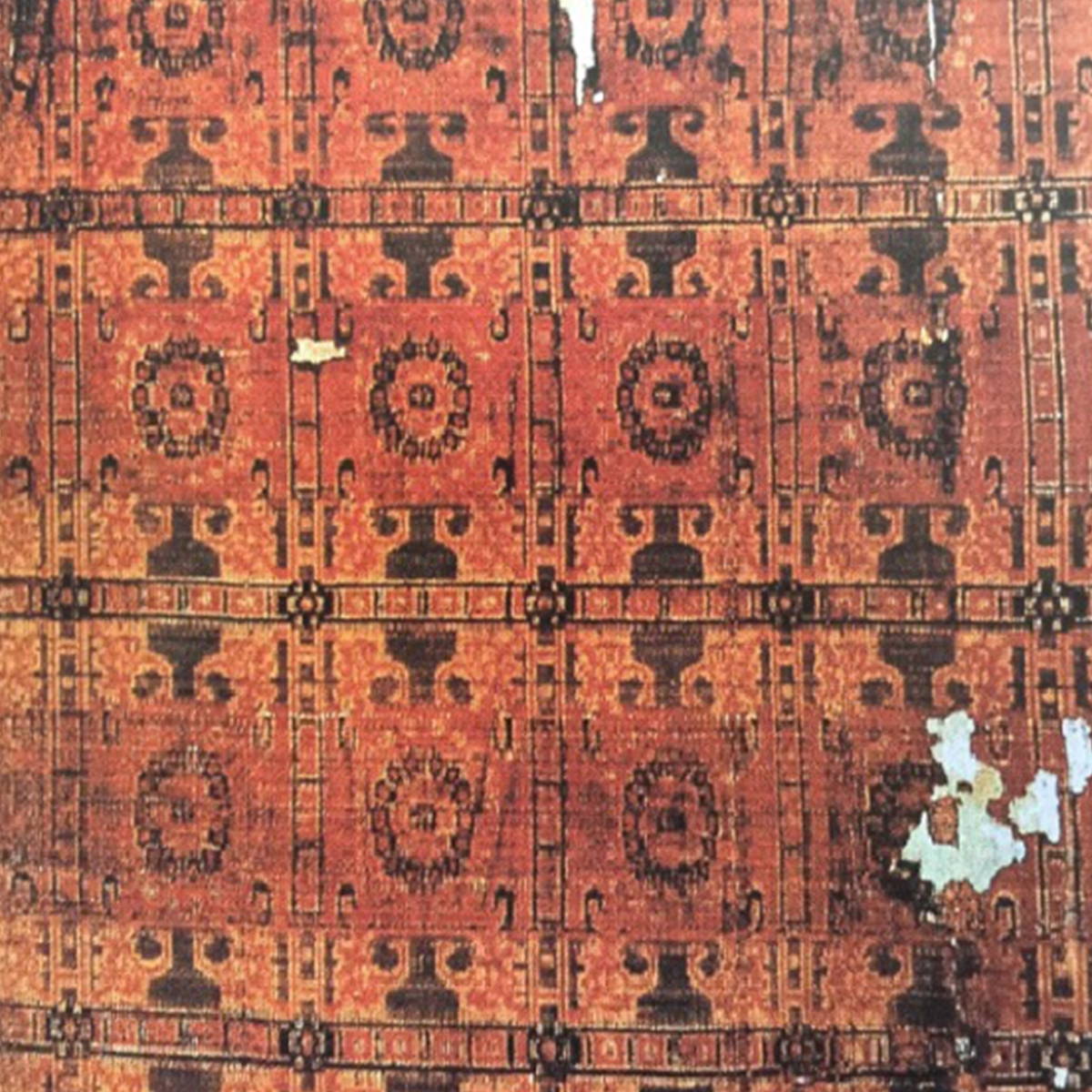A square product photograph of an orange and black woven textile with a geometric pattern, showing signs of wear and frayed edges, laid flat